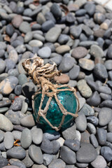 Vintage Japanese glass fishing floats and smooth gray pebbles piled together on a sandy beach by the ocean shore © Devka