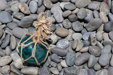Vintage Japanese glass fishing floats and smooth gray pebbles piled together on a sandy beach by the ocean shore © Devka