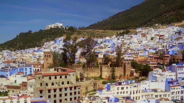 Drone orbits Chefchaouen's historic kasbah fortress amid blue medina and Rif Mountains.