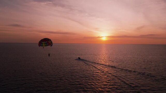 A colorful parasail and speedboat trail across a glowing tropical sunset sea