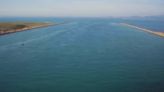 Drone advances through a harbor channel, the open sea stretching ahead.