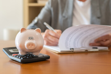 Fototapeta premium Piggy bank on calculator representing savings and careful financial planning for concepts like mortgage loans, home purchases, and real estate investments while reviewing documents
