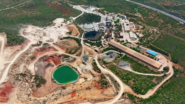 Cement production facility operates with quarry activities and aggregate processing. Heavy machinery transports raw materials through conveyor systems.
