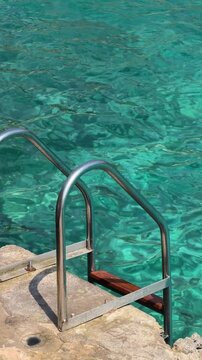 Metal ladder leading into crystal clear turquoise sea water, capturing a peaceful Mediterranean swimming spot on a sunny summer day in Mallorca.