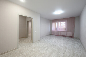 Fototapeta premium bright empty room with light beige walls, light wood laminate flooring, a window with sheer pink curtains, recessed ceiling lights, and an open doorway to another space
