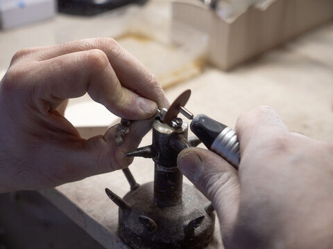 Dental technician polishing crown with rotary tool in prosthetic laboratory for restorative dentistry and dental prosthesis production.