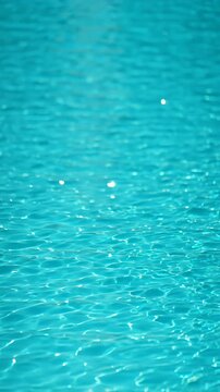 Clear turquoise water surface in a swimming pool sparkling in the sunlight with relaxing gentle ripples, creating a beautiful abstract liquid texture and a calm summer background