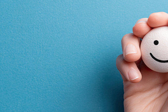 Hand holding happy smile face on blue background, Positive thinking, Mental health, World mental health day concept 