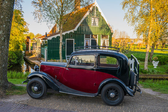 Vintage oldtimer car parked in front of traditional green Dutch house during golden hour