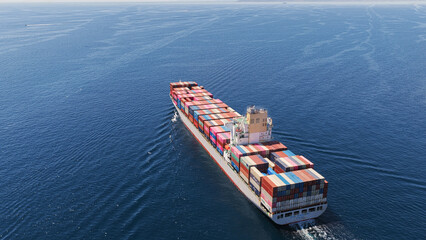 Container ship navigating across the vast blue ocean, carrying a full load of colorful cargo containers symbolizing global trade, international logistics, and maritime transport © Nasos Zovoilis