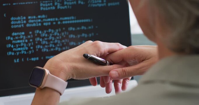 Female coder at desk seeing code on laptop, adjusting black pen and smartwatch, lifting to point