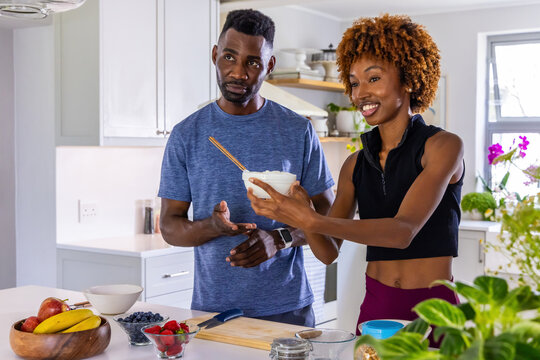 Couple preparing breakfast in modern home kitchen, woman offering white mixing bowl with spoon