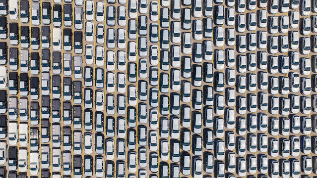 Overhead drone view of a vast parking lot packed with new black and white cars in neat parallel rows, illustrating automotive inventory, logistics and mass production storage