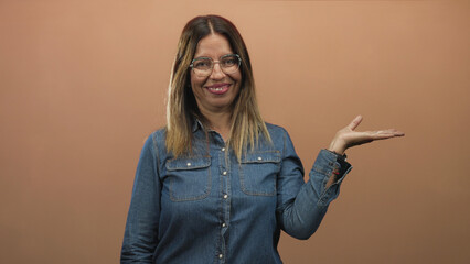 Fototapeta premium Woman wearing denim shirt and glasses holding palm up with open hand presenting an empty space in studio; confidence.