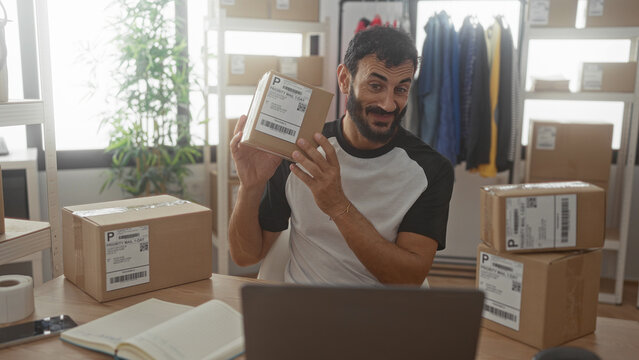 Man holding a package and stacking cardboard boxes at a packing table in a building; small business pride.