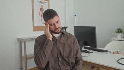 Fototapeta premium Man holding temples with both hands and closed eyes in a clinic building consultation room; pain concern.