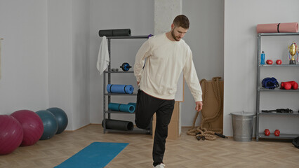 Fototapeta premium Man balancing on one leg on a yoga mat in a workout studio with exercise balls, ropes and dumbbells visible; focus balance calm.