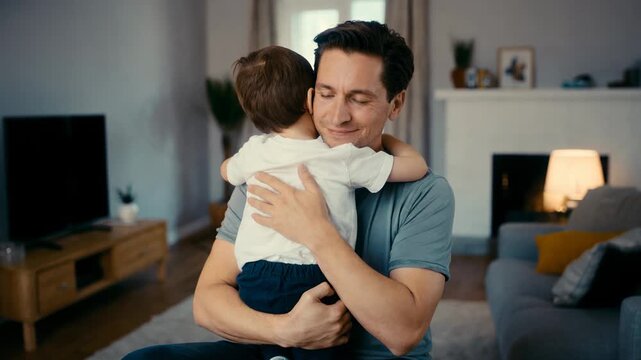 Father and young son hugging and embracing in living room with fireplace and soft lamp light