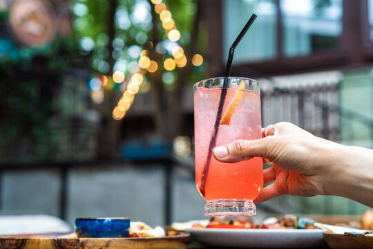 Cropped hand of a person holding a refreshing pink paloma cocktail at an outdoor restaurant terrace