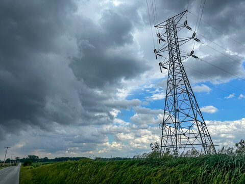 Dark storm clouds over a rural field and road by a high voltage electricity transmission tower in the American midwest