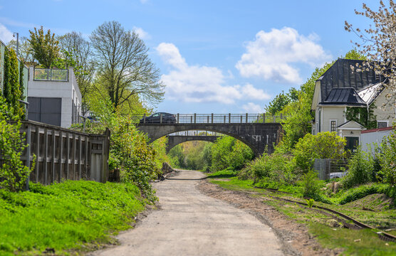 Quiet gravel road leading beneath bridge through green corridor.