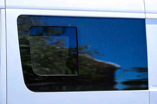 Tinted van side window reflecting trees and blue sky.