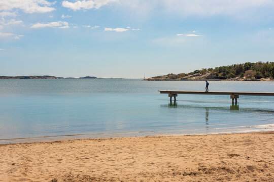 Person standing on pier overlooking calm sea and beach.