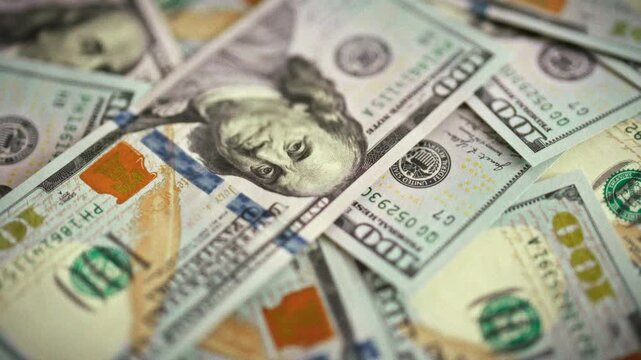 A top-down, daylight shot captures fresh hundred-dollar bills fanned across a table, their crisp cash glinting. The extreme close-up emphasizes money, highlighting finance and personal wealth