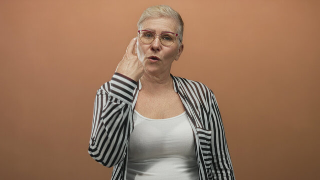 Woman with short grey hair and glasses showing two fingers for counting in studio against peach wall; confidence.
