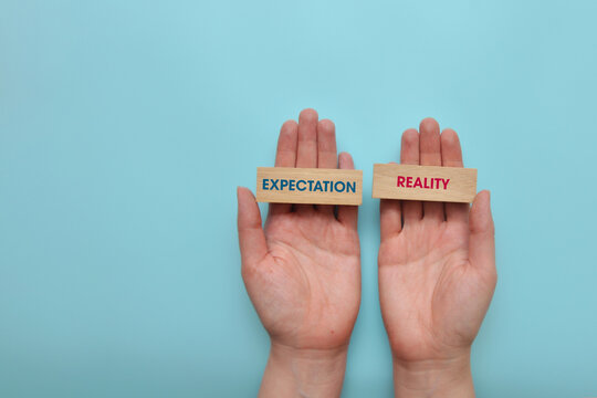 Expectation and reality labels held in hands on blue background