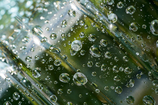 Water Droplets on Transparent Plastic Surface. Macro close-up of crystal-clear water droplets scattered across a transparent plastic surface with a soft green natural background.