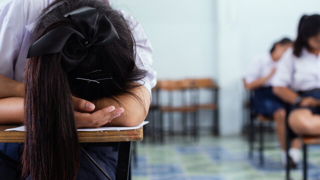 Exhausted Female Student Sleeping on Desk During Final Exam in Classroom
