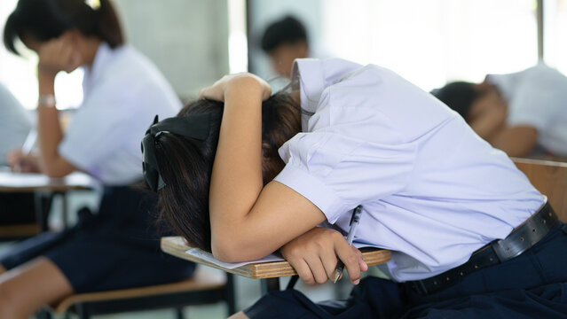Exhausted Female Student Sleeping on Desk During Final Exam in Classroom