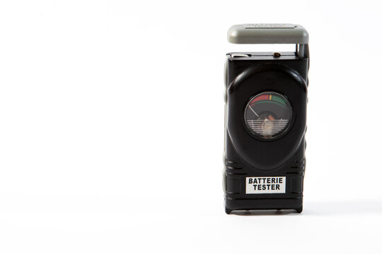 A vintage black portable analog battery tester with a german dial scale isolated on a clean white background