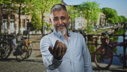 Naklejka premium Man extends hand toward camera beside parked bicycles on amsterdam street while smiling and beckoning; welcoming invitation.
