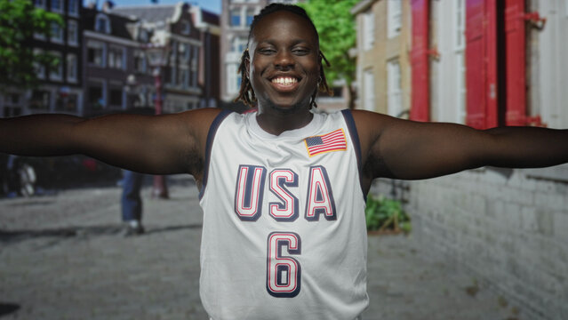 Man with arms outstretched smiling on a city street wearing a usa jersey with flag patch; joy celebration.