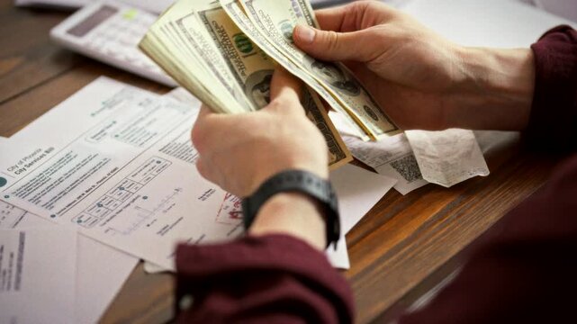At his desk, an aspiring entrepreneur tallies cash beside unpaid bills, using a calculator to gauge start-up capital. This moment captures early financial planning for launching a new business