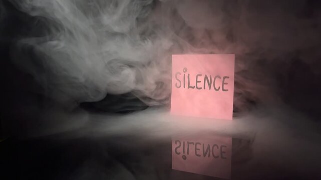 Pink note with the word &ldquo;SILENCE&rdquo; surrounded by smoke on a dark reflective background, symbolizing calm, mindfulness, boundaries, introspection, emotional space and the need for quiet.