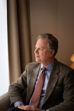 Thoughtful mature businessman looking through window in hotel room