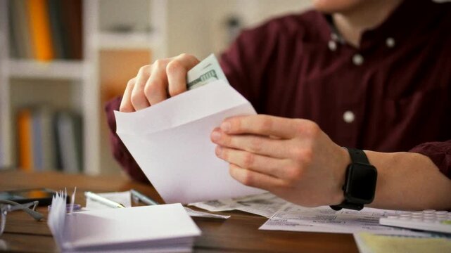 At his office desk, an accountant carefully slides cash into envelopes, surrounded by bills and a calculator, illustrating the meticulous, daylight-lit process of preparing employee salaries in cash