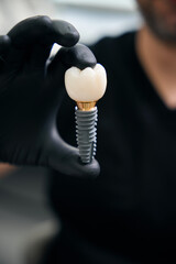 Adult man holding dental implant with ceramic crown indoors