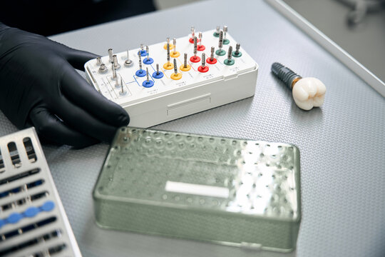 Hands in black gloves holding dental implant tools kit indoors