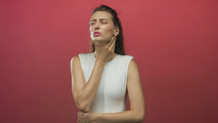 Obraz premium Woman clutching throat and holding neck with one hand in red studio wearing white sleeveless top and closed eyes; pain recovery.
