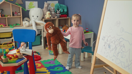 Little blonde girl hugging a large stuffed monkey with hands in a studio playroom  playful innocence. © Krakenimages.com