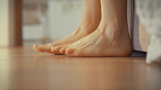 As morning arrives, man's bare feet slowly emerge from beneath covers, stretching his legs. He steps onto cool floor, marking start of new day, in serene awakening process showcasing morning routine