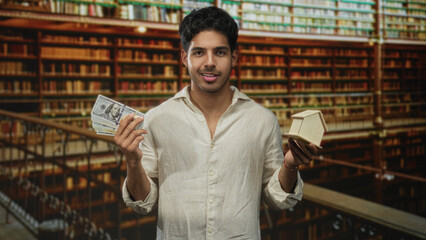 Fototapeta premium Man holding fanned cash in hands and a small wooden house model in a library building; financial planning ambition.