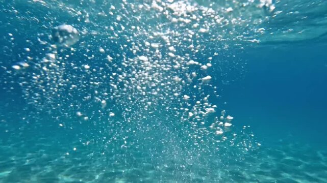 Underwater view of air bubbles rising in clear water above sandy bottom at midday