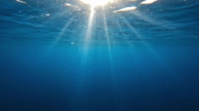 Underwater waves ripple and flow in deep blue ocean with light shining above during midday