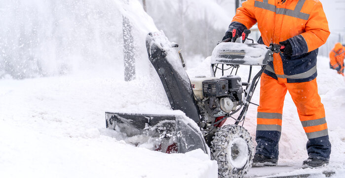 Worker clears snow with a snowblower in bright orange gear