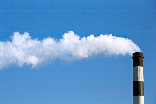 Tall industrial smokestack releases thick white plume into clear blue sky